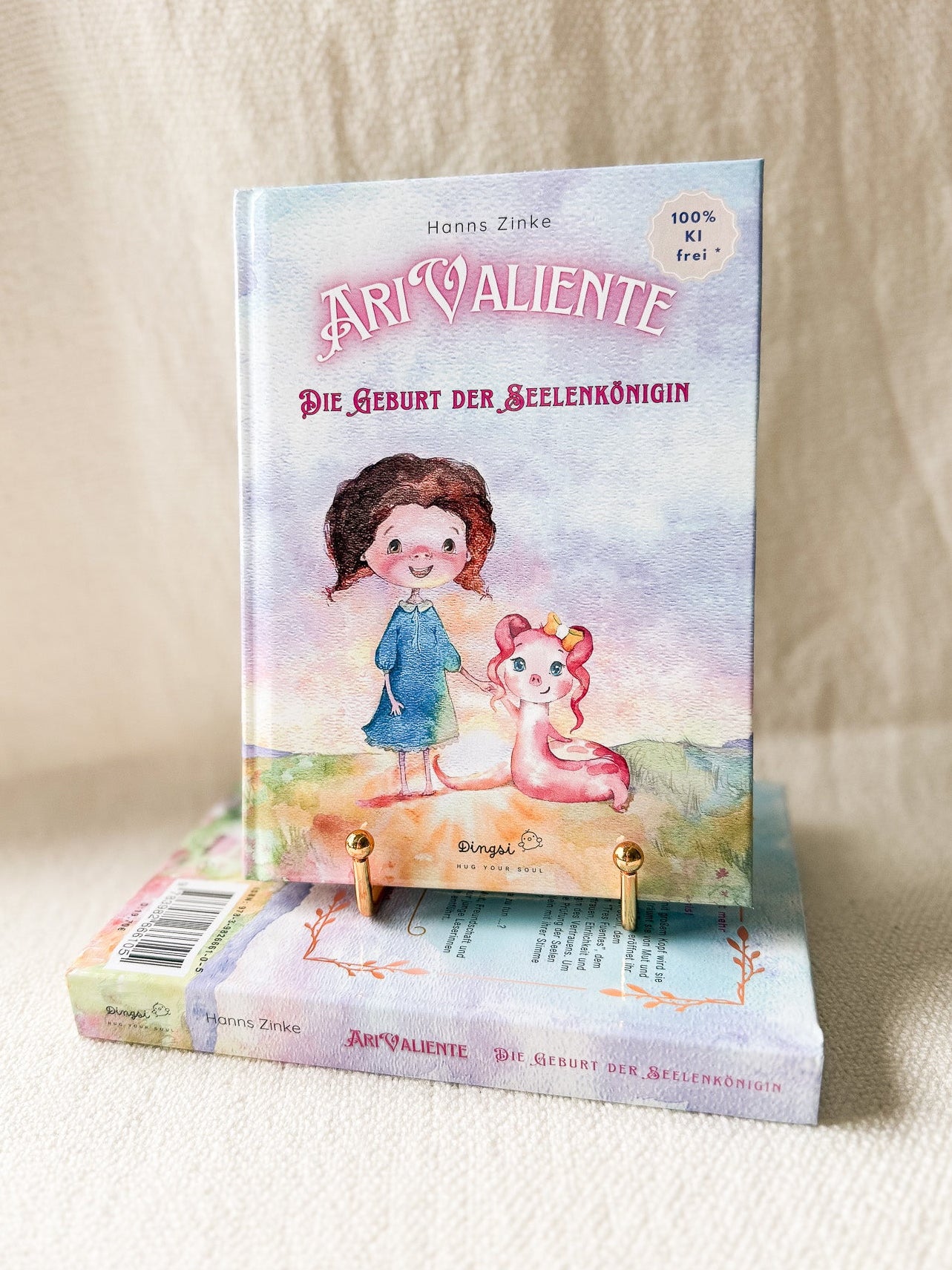 „Taschenbuch Ari Valiente – Die Geburt der Seelenkönigin von Hanns Zinke, liebevoll illustriertes Kinderbuch mit Fantasiefigur und Mädchen auf pastellfarbenem Cover, hochwertiges Produktfoto auf cremefarbenem Hintergrund.“